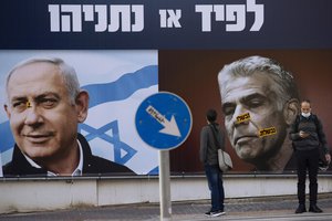 In this March 14, 2021, file photo, people stand in front of an election campaign billboard for the Likud party showing a portrait of its leader Prime Minister Benjamin Netanyahu, left, and opposition party leader Yair Lapid, in Ramat Gan, Israel.