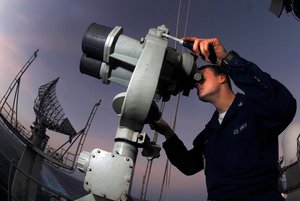 US Navy looks through binoculars for surface contacts while standing the port forward