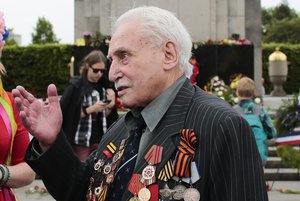 Soviet war veteran David Dushman, 92, center, talks to people holding Ukrainian flags as he attends a wreath laying ceremony