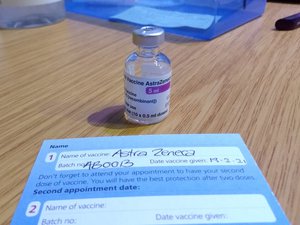 COVID-19 Vaccine AstraZeneca vial and NHS COVID-19 vaccination record card, ready on desk for injection at an NHS vaccination centre at the Bath Pavilion