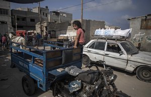 A Palestinian girl sits on an auto rickshaw next to a car loaded with sacks of flour received from the UN Relief and Works Agency, (UNRWA), at a warehouse in Gaza City, Wednesday, Sept. 30, 2020.