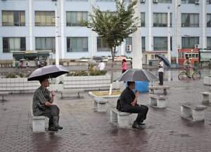 North Korean men use umbrella as they sit and watch a propaganda movie outside the train station in Pyongyang, North Korea