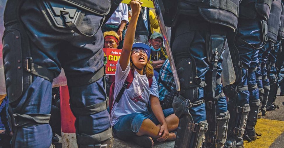 We shall not be moved! Anti-coup protesters remain seated in front of a line of riot police trying to clear roads in Yangon. Partially visible is a poster urging citizens to join the Civil Disobedience Movement.PANOS PICTURES