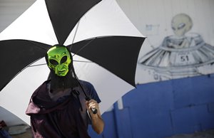 Seth Unterseher holds an umbrella for shade while wearing an alien mask at an event at the Little A'Le'Inn inspired by the "Storm Area 51" internet hoax Saturday, Sept. 21, 2019, in Rachel, Nev.