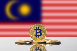 Set of four gold Bitcoin coins in front of the flag of the State of Malaysia