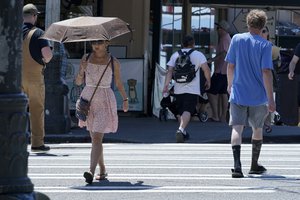 A person uses an umbrella for shade from the sun while walking near Pike Place Market, Tuesday, June 29, 2021, in Seattle