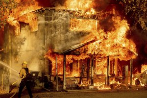 A firefighter sprays water while trying to stop the Sugar Fire, part of the Beckwourth Complex Fire, from spreading to neighboring homes in Doyle, Calif., Saturday, July 10, 2021. Pushed by heavy winds amid a heat wave, the fire came out of the hills and destroyed multiple residences in central Doyle.