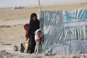 An internally displaced Afghan woman stands with her daughters in front a makeshift tent in a camp on a rocky patch of land, after fleeing fighting between the Taliban and Afghan security personnel, on the edge of the city of Mazar-e-Sharif, northern Afghanistan, Thursday, July 8, 2021.