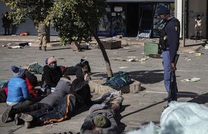 A policeman watches over arrested looting suspects at a shopping centre, in Soweto near Johannesburg, Tuesday July 13, 2021 as ongoing looting and violence continues