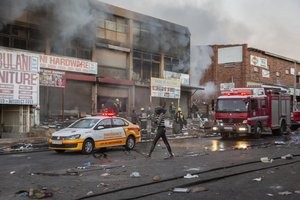 A woman walks past a fire truck as it extinguishes flames in a looted store in Alexandra township, Johannesburg, South Africa, Monday, July 12, 2021