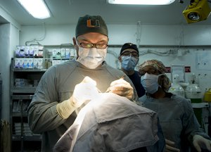 Lt. Cmdr. Howard Pryor, a Navy doctor, makes an incision into an epidermal inclusion cyst on the head of a patient in the surgery room of the Nimitz-class aircraft carrier USS Abraham Lincoln (CVN 72).