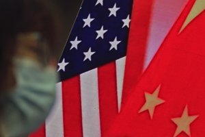 FILE - In this Feb. 22, 2021, file photo, a woman wearing a face mask to help curb the spread of the coronavirus sits near a screen showing China and U.S. flags as she listens to a speech by Chinese Foreign Minister Wang Yi at the Lanting Forum on bringing China-U.S. relations