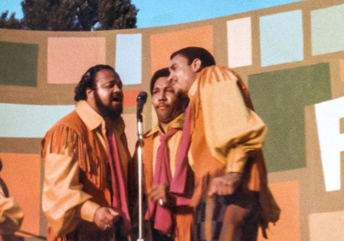 Summer of Soul film still: Three singers lean in to one microphone stand