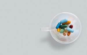 Assorted and colorful medication pill tablets and capsules in a transparent coffee cup