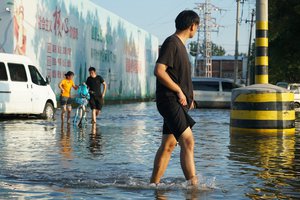 People walk along a flooded street in Xinxiang in central China's Henan Province, Monday, July 26, 2021