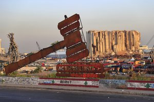 A justice symbol monument is seen in front towering grain silos that gutted in the massive last year August explosion at the Beirut port that claimed the lives of more than 200 people, in Beirut, Lebanon, Wednesday, Aug. 4, 2021. A year after the deadly blast, families of the victims are consumed with winning justice for their loved ones and punishing Lebanon's political elite