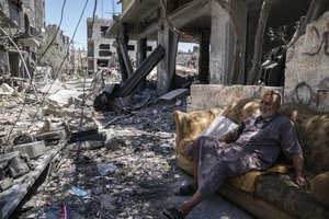 Mofeed Sabit, 64, sits on a couch along a road covered in debris, from an airstrike that destroyed a building prior to a cease-fire reached after an 11-day war between Gaza's Hamas rulers and Israel, Monday, May 24, 2021, in Magazzi, the Gaza Strip.