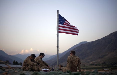 In this Sept. 11, 2011 file photo, US soldiers sit beneath an American flag just raised to commemorate the tenth anniversary of the 9/11 attacks at Forward Operating Base Bostick in Kunar province, Afghanistan.