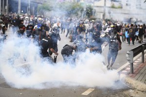 An anti-government protester tries to control smoke from a tear gas canister fired by riot police during a protest in Bangkok, Thailand, Friday, Aug. 13, 2021