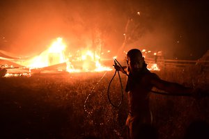 A man uses a water hose during a wildfire in Adames area, in northern Athens, Greece, Tuesday, Aug. 3, 2021.