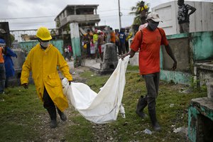 Men carry the body of a boy that was found in collapsed building lies at the back of a truck at the entrance of the cemetery in Les Cayes, Haiti, Tuesday, Aug. 17, 2021