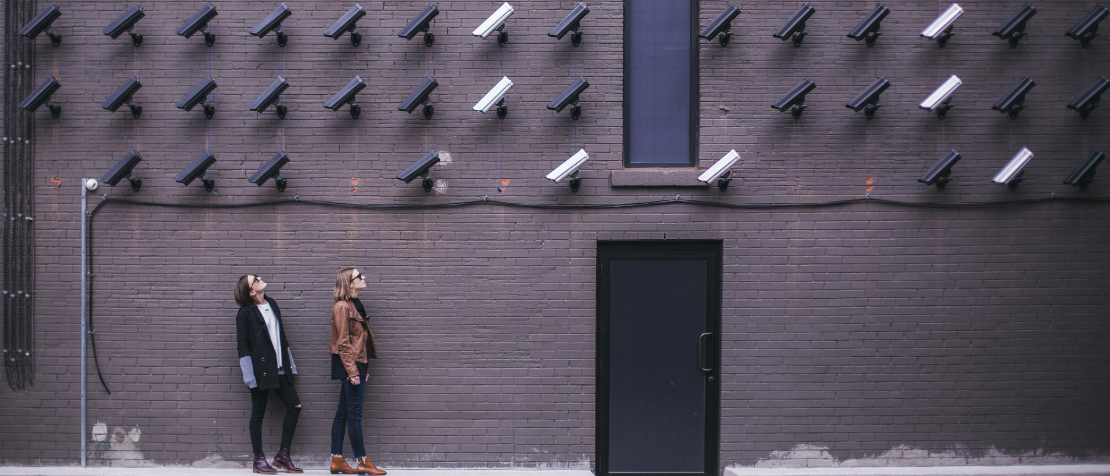 photo of 2 women in a street looking up at a wall of surveillance cameras