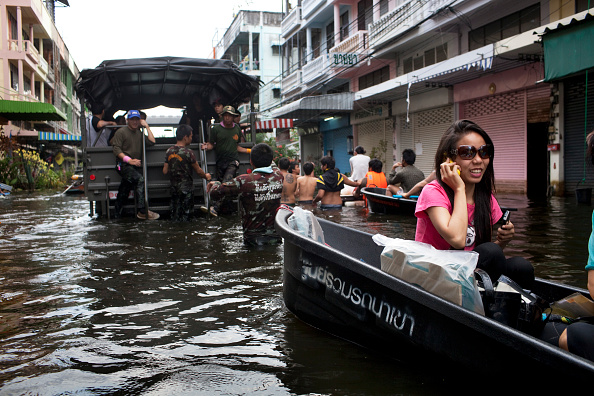 The image shows a flood street with people evacuating on two boats and a truck.