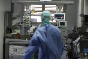 In this March 16, 2020, photo, a doctor watches a coronavirus patient under treatment in the intensive care unit of the Brescia hospital, Italy.