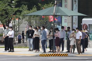 People wearing face masks as a precaution against the coronavirus stand under a shade canopy as they wait to cross a road in Seoul, South Korea, Tuesday, Aug. 3, 2021