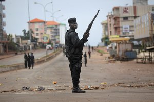 Guinean police carrying a gun stand as they clear the mostly Peul suburb of Bambeto in Conakry, Guinea, Tuesday, Nov. 16, 2010, as groups of UFDG youth set up barricades.