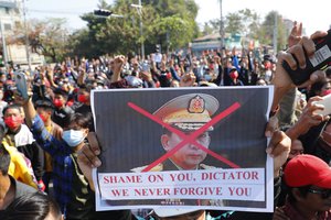 A protester holds a placard with a defaced image of Myanmar military Commander-in-Chief Senior Gen. Min Aung Hlaing during a protest in Mandalay, Myanmar, Tuesday, Feb. 9, 2021