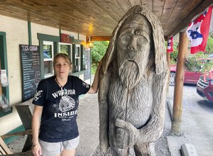 File - Pauline Bauer leans against a wooden statue outside Bob’s Trading Post, her restaurant in Hamilton, Pa., Wednesday, July 21, 2021. Bauer is one of more than 540 people charged with federal crimes stemming from the Jan. 6 riot at the U.S. Capitol.