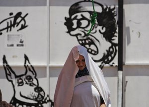 Libyan woman prays in front of graffiti depicting Libyan leader Moammar Gadhafi during Friday prayers in the rebel-held Benghazi, Libya, Friday, July 1, 2011.