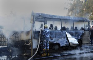 In this photo released by the Syrian official news agency SANA, shows a Syrian firefighter extinguishes a burned bus at the site of a deadly explosion, in Damascus, Syria, Wednesday, Oct. 20, 2021.