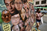 A woman walks past a banner with photos of pro-democracy activists including Jimmy Lai, left, who was arrested by police in 2020, during the anniversary of the Hong Kong handover to China from Britain in Hong Kong, Thursday, July 1, 2021.