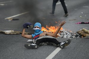 An anti-government protester lies in front of a burning barricade in an attempt to block traffic, in Caracas, Venezuela, Saturday, Nov. 16, 2019