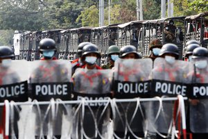 In this Friday, Feb. 19, 2021 file photo, military trucks with soldiers inside are parked behind police standing guard behind a road barricade in Mandalay, Myanmar.