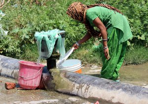 File - A woman fills a water bucket with water from a public G.I pipe amidst a water shortage in Jammu, India.