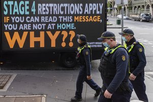 Victorian protective service officers are seen walking on patrol past a sign reading 'Stage 4 restrictions apply, if you can read this message, you are not at home, why?' as lockdown of Melbourne forces people to stay at home if not working due to the continuing spread of COVID-19, Wednesday, Aug. 5, 2020.