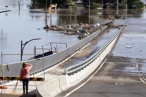 FILE - In this March 25, 2021, file photo, a woman looks at debris caught on a submerged bridge in Windsor, northwest of Sydney, Australia.