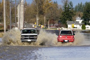 Pickup trucks send up plumes of muddy water as they pass on a flooded road, Tuesday, Nov. 16, 2021, near Everson