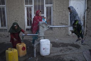 Girls fill containers with water using a hand pump at a camp for internally displaced people, in Kabul, Afghanistan, Monday, Nov. 15, 2021.