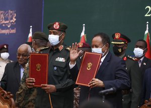 In this photo provided by the Sudan Transitional Sovereign Council, Sudan's top general Abdel Fattah Al-Burhan, center left, and Prime Minister Abdalla Hamdok hold documents during a ceremony to reinstate Hamdok, who was deposed in a coup last month, in Khartoum, Sudan, Sunday Nov. 21, 2021