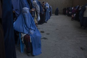 An Afghan woman sits on a chair as she waits with others to receive cash at a money distribution organized by the World Food Program in Kabul, Afghanistan, Saturday, Nov. 20, 2021.