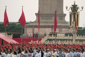 Communist party members wave flags as an honor guard prepares to raise the national flag during a ceremony to mark the 100th anniversary of the founding of the ruling Chinese Communist Party at Tiananmen Gate in Beijing Thursday, July 1, 2021.