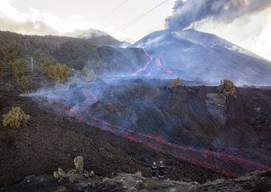 Firefighters look at lava flowing from a volcano on the Canary island of La Palma, Spain, Tuesday, Nov. 30, 2021