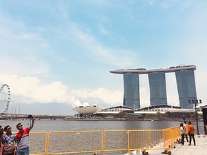 Tourists taking selfies along Merlion Park. Singapore Flyer, Marina Bay Sands, and ArtScience Museum can be seen across the bay, in Singapore. Taken on September 2018.