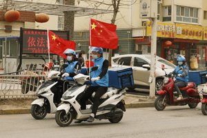 Delivery workers flying Chinese national flags ride around in a convoy to promote their services in Shule county in northwestern China's Xinjiang Uyghur Autonomous Region on March 20, 2021