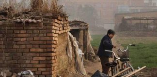 Image from Liang Village, a woman pulls a trolley next to brick.