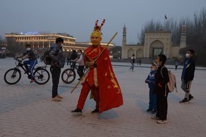 A performer dressed as the monkey god from a Chinese fable walks near a mosque as Uyghur children gaze upon him Kashgar in northwestern China's Xinjiang Uyghur Autonomous Region on Friday, March 19, 2021